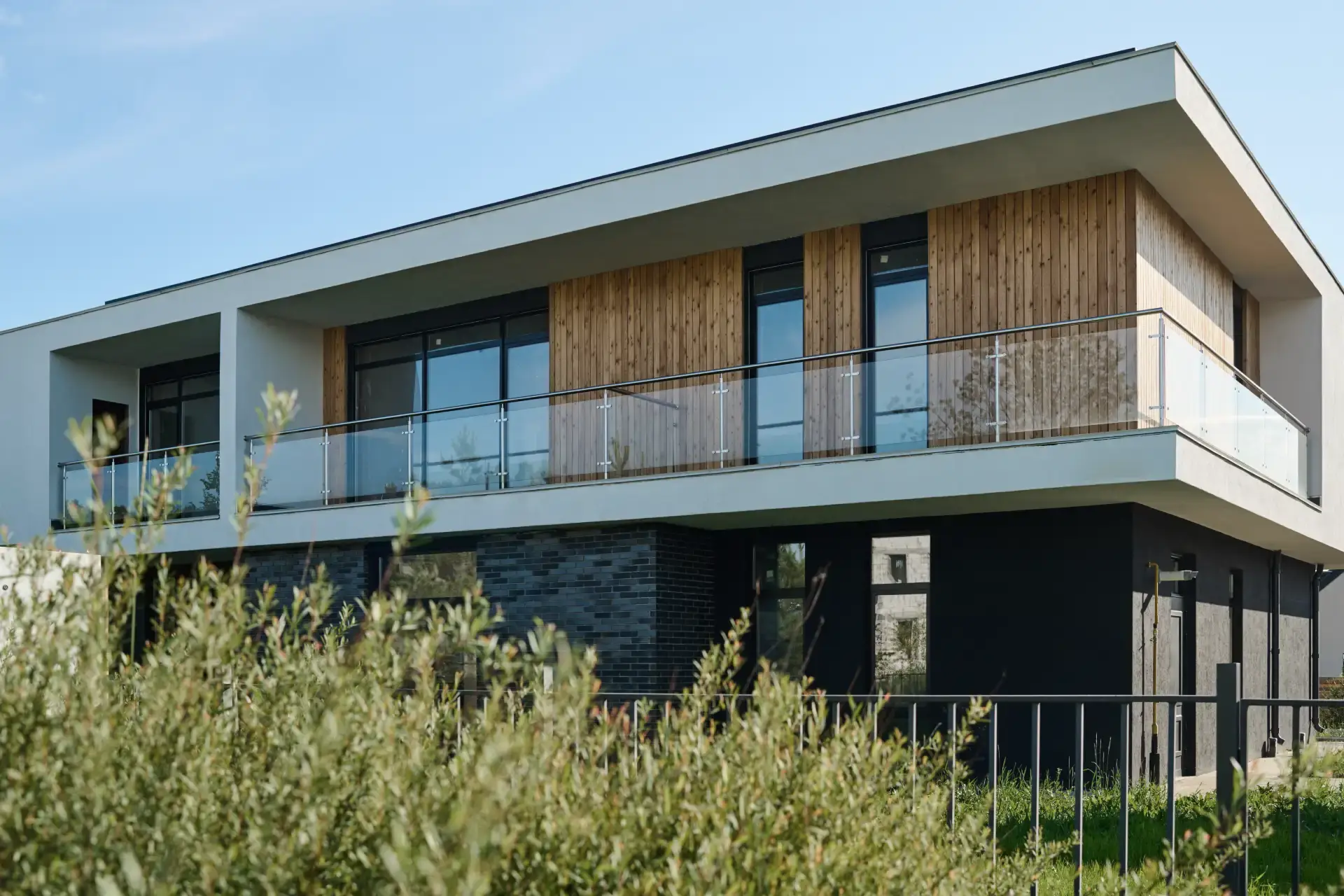 A modern two-storey home with dark brick, wood cladding and a glass balcony